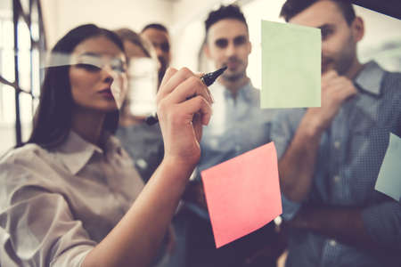 Beautiful business people are using stickers and marker, discussing ideas and smiling during the conference in officeの写真素材