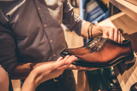 Cropped image of beautiful couple choosing classic shoes while doing shopping in the male store