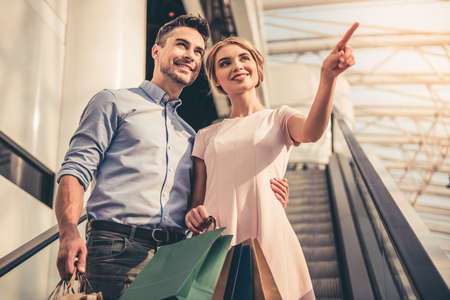 Beautiful couple with shopping bags is talking and smiling while doing shopping in the mallの写真素材
