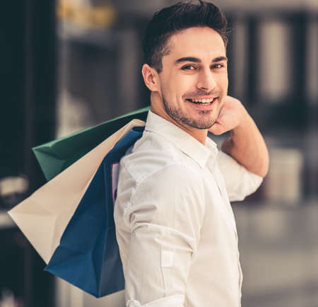 Handsome guy with shopping bags is looking at camera and smiling while doing shopping in the mallの写真素材
