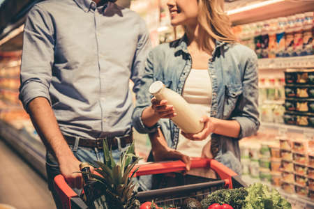 Beautiful couple is talking and smiling while doing shopping at the supermarketの写真素材