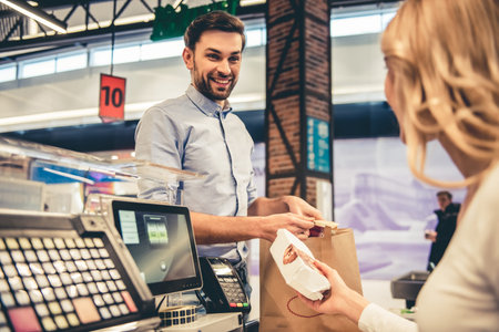 Handsome man is smiling while standing at the cash desk in the supermarketの写真素材