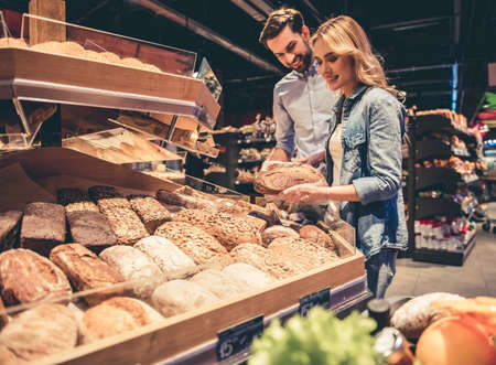 Beautiful young couple is choosing baking and smiling while doing shopping at the supermarketの写真素材