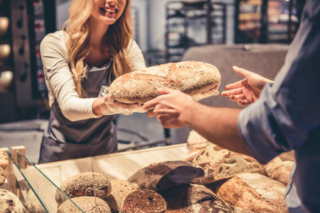 At the supermarket. Cropped image of beautiful young female worker offering a bread to the customer...