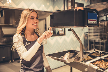 At the supermarket. Beautiful young female worker is weighing fish and smilingの写真素材