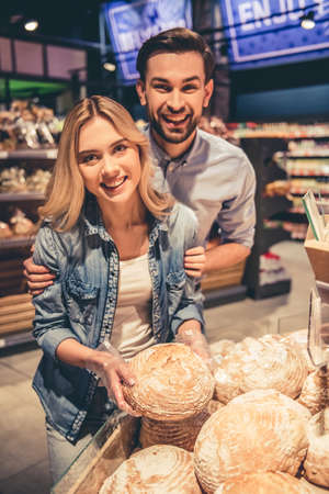 Beautiful young couple is choosing baking and smiling while doing shopping at the supermarketの写真素材