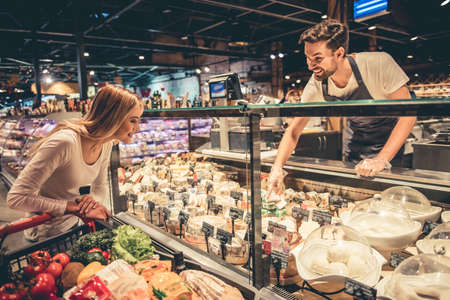 At the supermarket. Handsome worker is offering cheese to the beautiful customer and smilingの写真素材