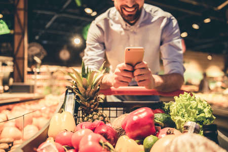 Cropped image of handsome man using a mobile phone and smiling while doing shopping at the supermarketの写真素材