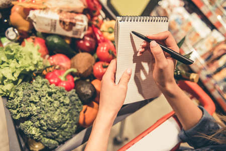Cropped image of beautiful young woman holding a list of goods while doing shopping at the supermarketの写真素材