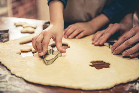 Cropped image of little girl and her mom in aprons preparing cookies using cookie cutters in the kitchenの写真素材