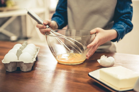 Cropped image of cute little girl in apron whisking eggs for baking in the kitchen