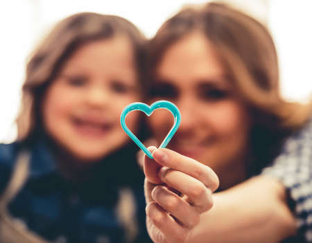 Cute little girl and her beautiful young mom are holding a heart-shaped cutter and smiling while baking in kitchenの写真素材