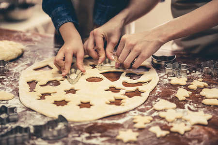 Cropped image of little girl and her mom in aprons preparing cookies using cookie cutters in the kitchenの写真素材