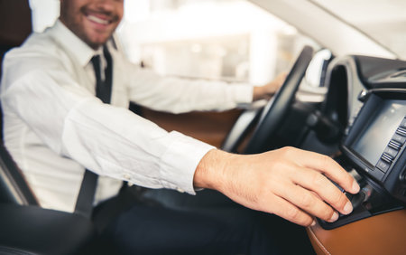 Cropped image of handsome businessman in suit smiling while sitting in a new car in car dealership