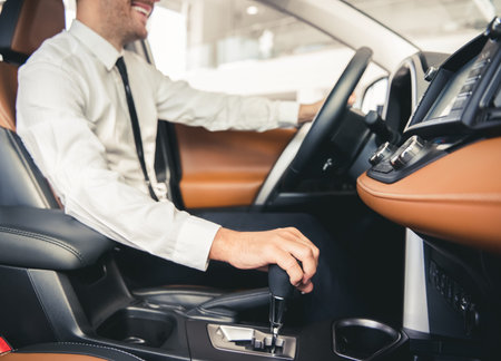Cropped image of handsome businessman in suit smiling while sitting in a new car in car dealership