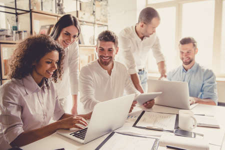 Successful young business people are using gadgets, sharing ideas and smiling while working in officeの写真素材