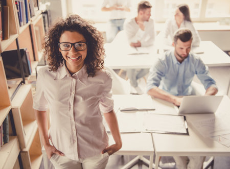Successful young business people are working in office. Girl in the foreground is looking at camera...
