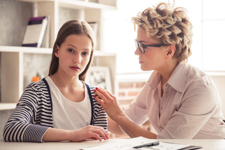 Teenage girl is visiting psychotherapist, they are talking during the session in office