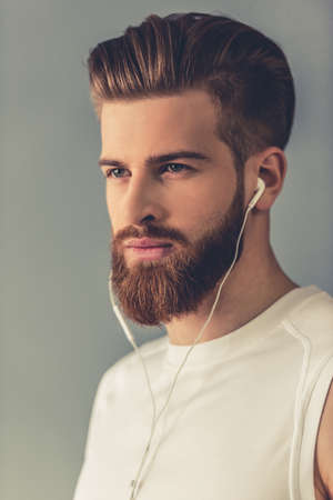 Portrait of handsome young bearded sportsman in earphones, on gray backgroundの写真素材