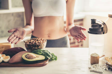 Cropped image of beautiful young sportswoman lifting hands in dismay while choosing between sport supplements and healthy foodの写真素材