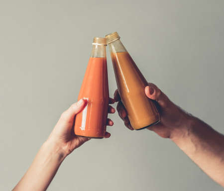 Cropped image of young sports people holding nutritious cocktails, on gray backgroundの写真素材