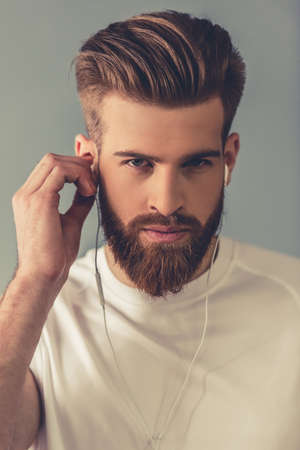 Portrait of handsome young bearded sportsman in earphones, on gray backgroundの写真素材