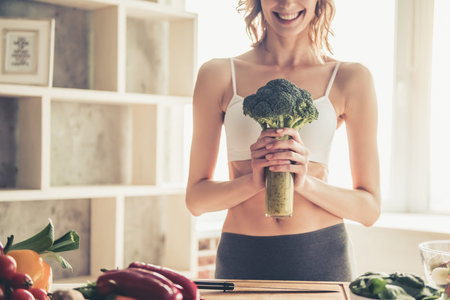 Beautiful young sportswoman is smiling while cooking healthy food in kitchen at homeの写真素材