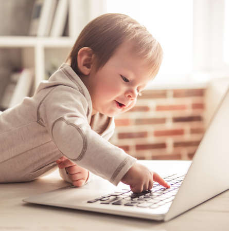 Cute baby boy is playing with laptop and smiling while lying on the table at homeの写真素材