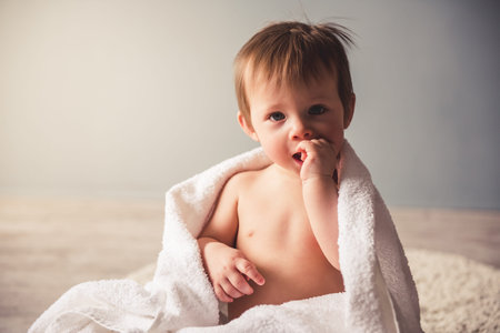 Cute baby boy in diaper is smiling while sitting on the carpet at homeの写真素材