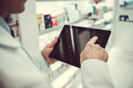 Cropped image of handsome pharmacist using a digital tablet while checking medications in pharmacyの写真素材