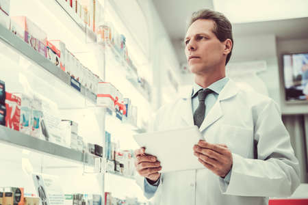 Handsome pharmacist is using a digital tablet while checking medications in pharmacyの写真素材