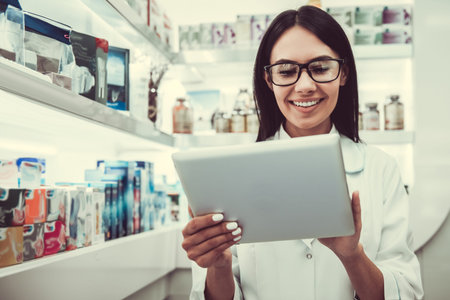Beautiful female pharmacist is using a digital tablet and smiling while working in pharmacyの写真素材
