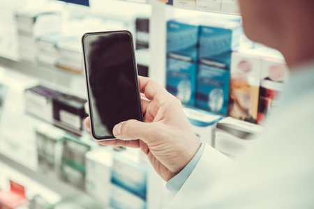 Cropped image of handsome pharmacist using a smart phone while working in pharmacyの写真素材