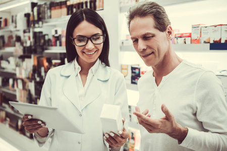 Beautiful young female pharmacist is suggesting a medication to a client at the pharmacy, holding a digital tablet and smilingの写真素材