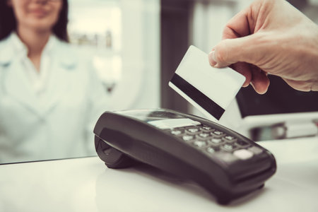 At the pharmacy. Cropped image of young female pharmacist working at the cash desk, client is paying...