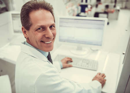 Handsome pharmacist is looking at camera and smiling while working with a computer at the pharmacyの写真素材
