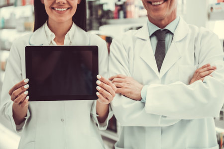 Beautiful pharmacists are holding a digital tablet and smiling while working in pharmacy