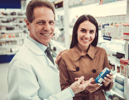 Handsome pharmacist is offering a medication to a beautiful young female client at the pharmacy, both are smilingの写真素材