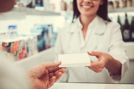At the pharmacy. Beautiful young female pharmacist is offering a medication to a client while working at the cash deskの写真素材