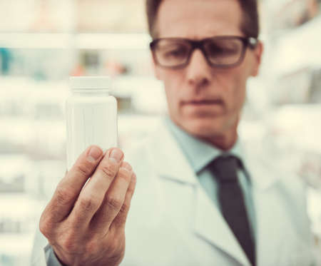 Handsome pharmacist is holding a medication while working in pharmacyの写真素材