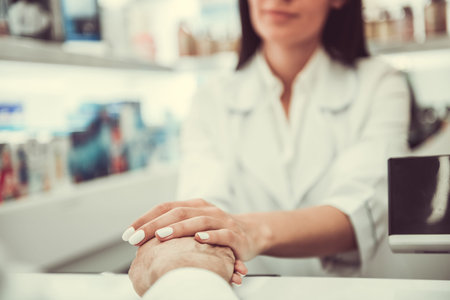 At the pharmacy. Beautiful young female pharmacist is holding a client's hand and supporting him while working at the cash deskの写真素材