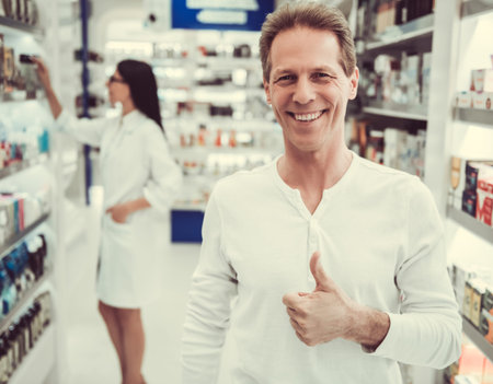 At the pharmacy. Handsome client is showing Ok sign and smiling, beautiful female pharmacist in the backgroundの写真素材