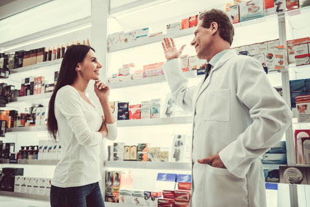 Handsome pharmacist is offering a medication to a beautiful young female client at the pharmacy, both are smilingの写真素材