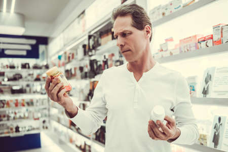 At the pharmacy. Handsome client is searching for a medication, choosing between twoの写真素材