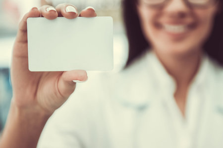 At the pharmacy. Cropped image of young female pharmacist holding a card and smiling, card in focusの写真素材