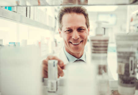 Handsome pharmacist is smiling while searching for medications in pharmacyの写真素材
