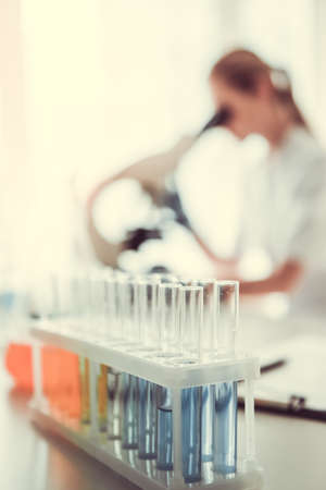 At the laboratory. Test tube with substances in the foreground, doctor is using a microscope in the backgroundの写真素材