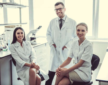Beautiful medical doctors are looking at camera and smiling while working at the labの写真素材