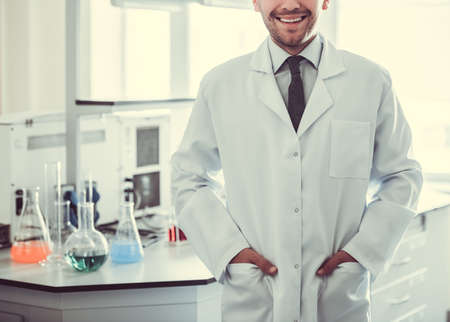 Handsome medical doctor in white coat is smiling while standing in laboratoryの写真素材