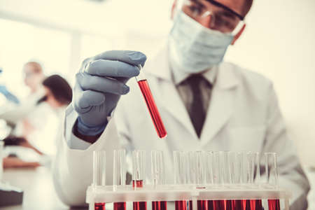 Handsome medical doctor in gloves and mask is working with test tubes at the labの写真素材
